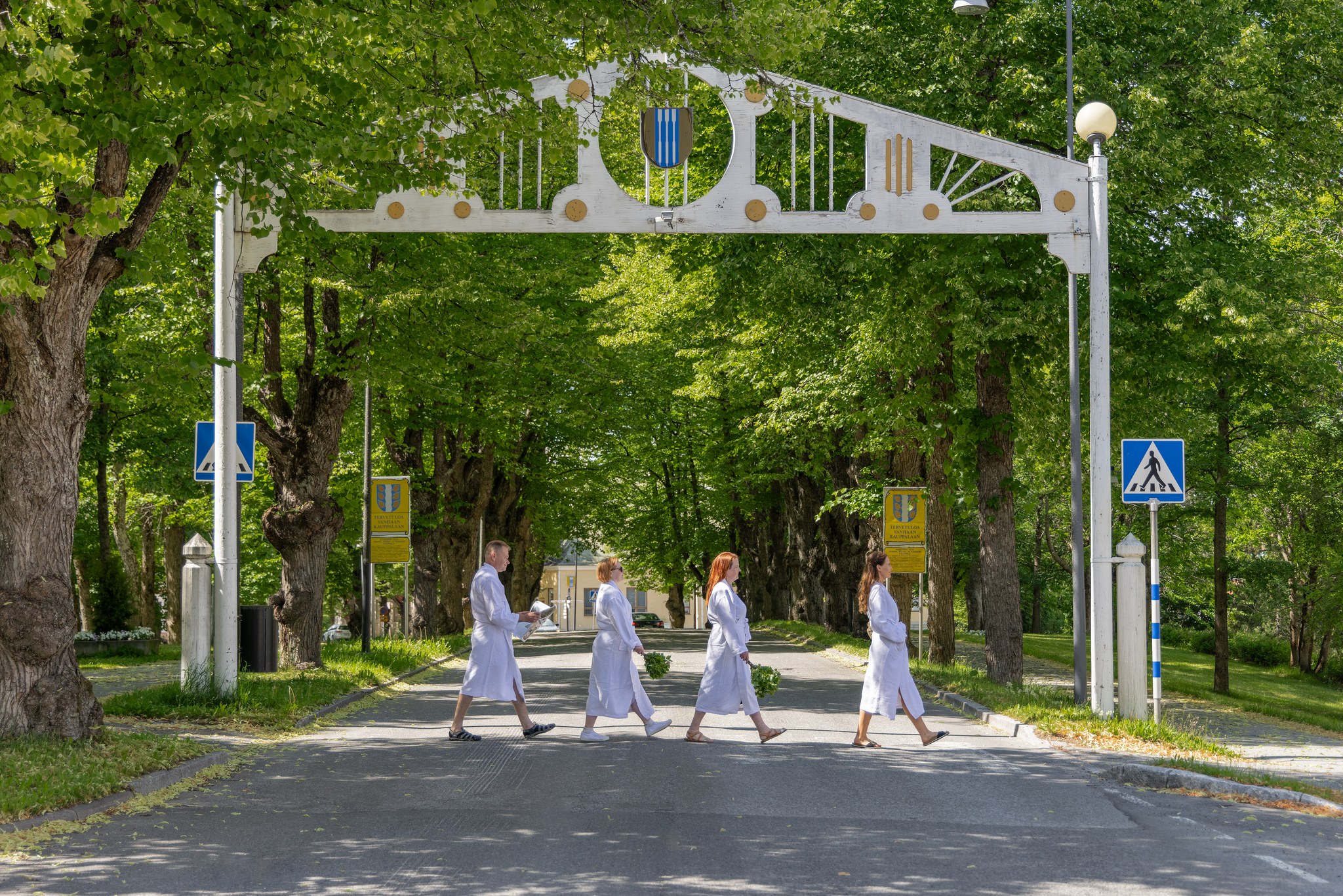 Neljä ihmistä kylpytakeissa kävelee vanhassa kauppalassa.